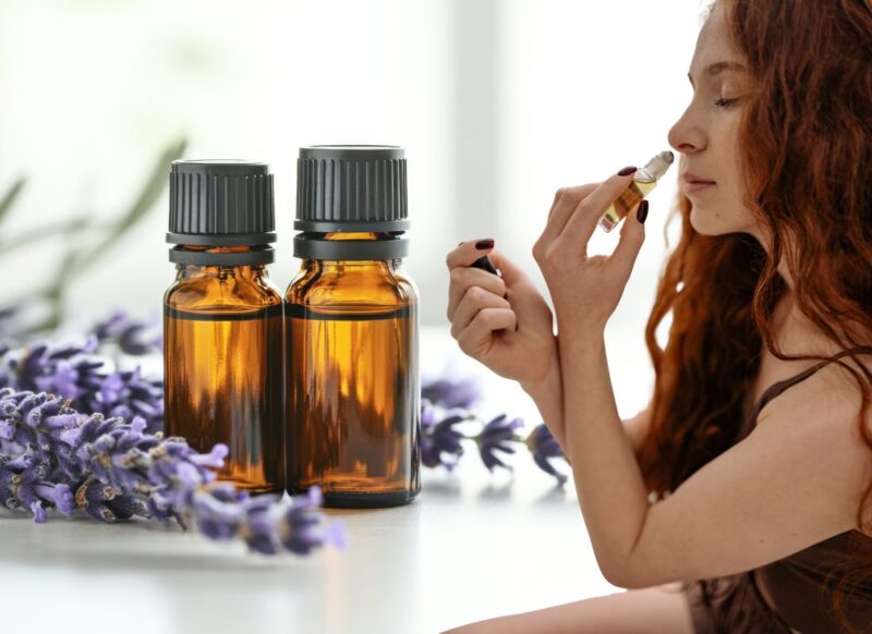 devojka miriše ulje laavnde, u pozadini 2 bočice ulja lavande i lavanda okolo